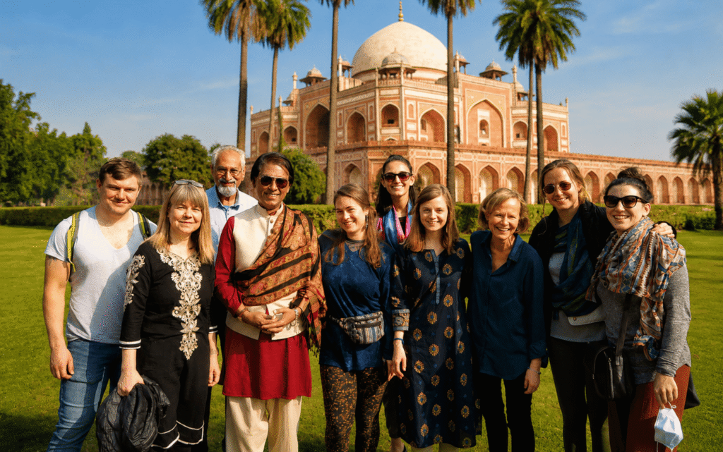 A local expert guiding a group of international travelers through the lush green pathways and water channels of the Charbagh gardens.