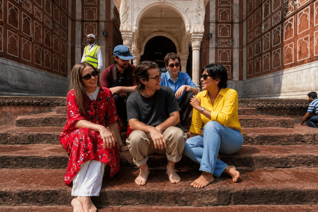 Jama Masjid Tour Guide – History, Timings & Best Experience 5 Tourists and worshippers sitting by the pool at the white marble canopy near the main arch of Jama Masjid under a clear sky