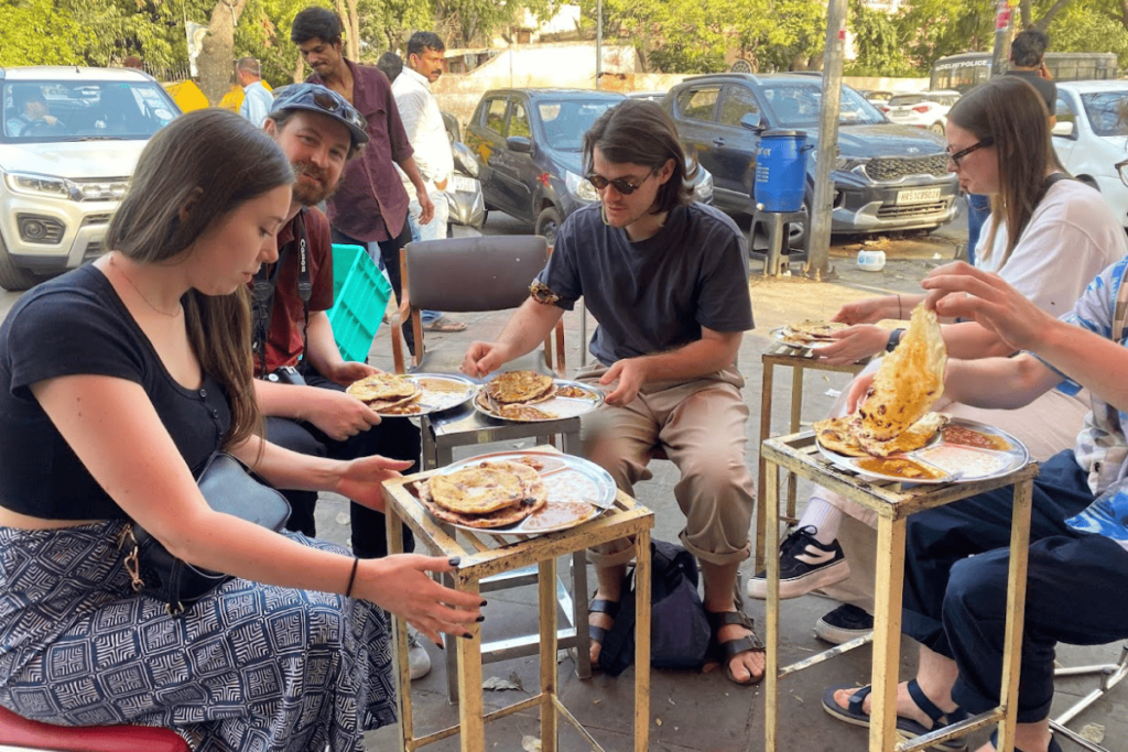 Harry, the Mathura Vrindavan tour guide, enjoying a delightful vegetarian meal with her guests, savoring traditional dishes like dal, chapati, rice, and Mathura ke peda in a local eatery, sharing the flavors of satvik cuisine.