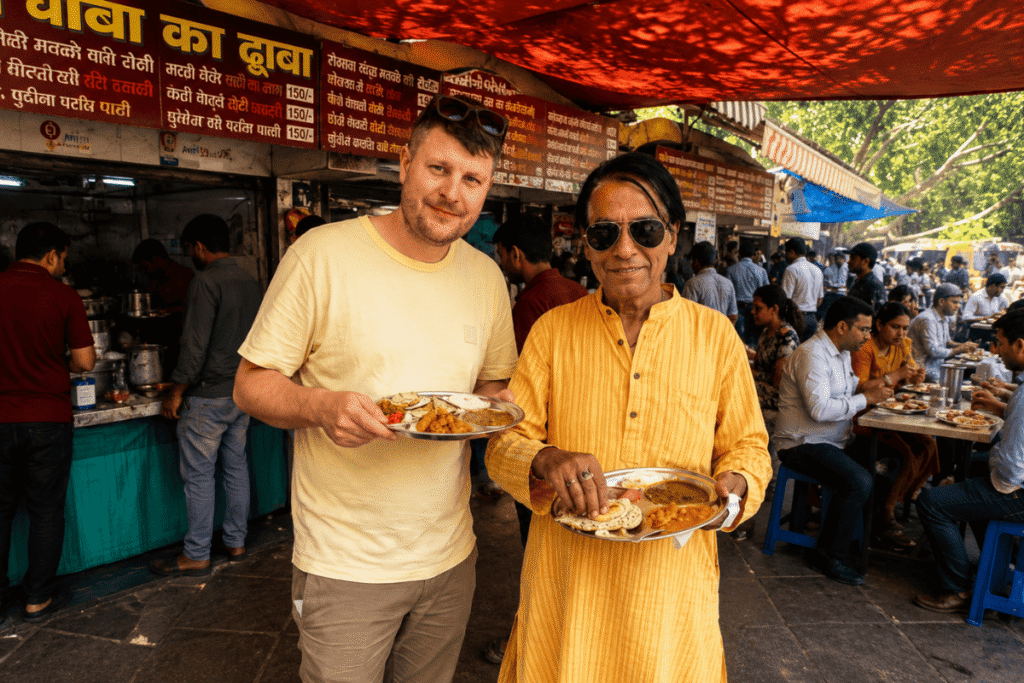 International tourist David and Delhi tour guide Harry holding traditional steel plates of authentic Indian street food at a local dhaba restaurant